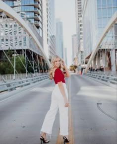 a woman standing on the side of a road in front of tall buildings with her hands behind her head