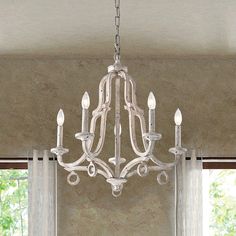 a white chandelier hanging from a ceiling in a room with curtains and windows