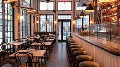 an empty restaurant with tables and chairs in front of large windows, lit by hanging lights