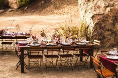 an outdoor table set up with place settings and flowers on it for a dinner party