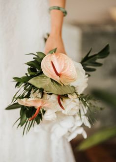 a bride holding a bouquet of flowers in her hand with greenery on the side