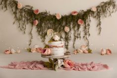 a wedding cake with pink flowers and greenery on the wall in front of it