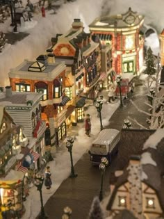 a toy town with lots of buildings and lights in the snow at night time,