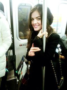 a woman standing on a subway car holding onto the pole with one hand and smiling at the camera