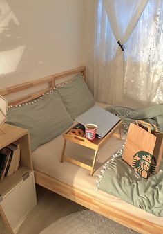 a small bed with a laptop on top of it next to a book shelf and window