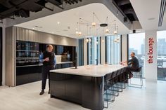 two men are standing in the middle of a large kitchen with an island and bar stools