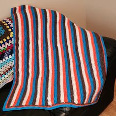 a crocheted blanket sitting on top of a black leather couch next to a pillow