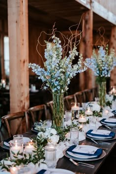 the table is set with blue and white plates, silverware, candles and flowers