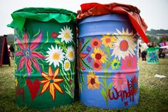 two colorful trash cans sitting on top of a grass covered field next to each other