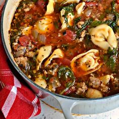 a pot filled with pasta and spinach soup on top of a red towel next to a wooden spoon