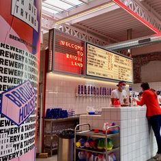 two men are standing at the bar in front of menus and drinks on the wall