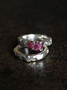 A unique ring with an uncut ruby complete with a sterling silver band. A unique ring with a unique stone - a raw ruby from Tanzania. The stone has an irregular shape and a dark pink color. Here and there you can see metallic inclusions of rutile, which makes this stone even more original. The approximate dimensions of the stone are 7 x 11 mm. The set includes a sterling silve ring with a texture matching the ring band, reminiscent of the raw texture of a rock. I designed the ring in such a way that its form emphasized the severity of the ruby. The thickness of the ring strip and the band varies between 3-5 mm.  I made the ring and wedding ring by hand from 925 silver using the sand casting technique.  This is a unique product, made in one piece in size 12 EU/6 US (internal diameter 16,5 mm Hand Forged Ruby Ring In Red, Hand Forged Ruby Ring Jewelry, Hand Forged Red Ruby Ring, Sterling Silver Wedding Rings With Raw Stone, Wedding Rings With Raw Stone In Sterling Silver, Hand Forged Sterling Silver Ruby Ring, Silver Ruby Birthstone Promise Ring, Anniversary Ruby Rings Hand Forged, Anniversary Hand Forged Ruby Rings