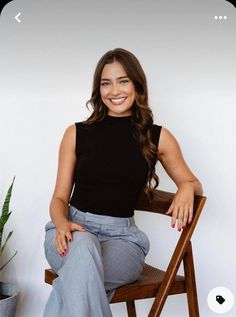 a woman sitting on top of a wooden chair next to a potted plant and smiling