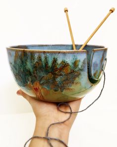 a hand holding a bowl with two knitting needles in it