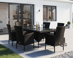 an outdoor dining table and chairs in front of a white house with black glass doors