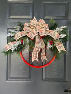 a christmas wreath hanging on the front door with ribbons and bows attached to it's sides