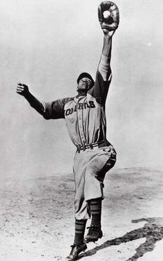 an old black and white photo of a baseball player holding a glove in the air