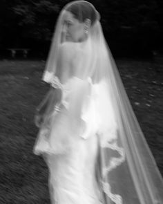 a woman in a wedding dress and veil walking through the grass with her hand on her hip