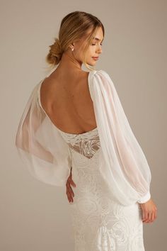 a woman in a white wedding dress with sheer sleeves and an open back, looking at the camera