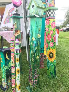 several colorful birdhouses are on display in the grass at an outdoor event with flowers and butterflies painted on them