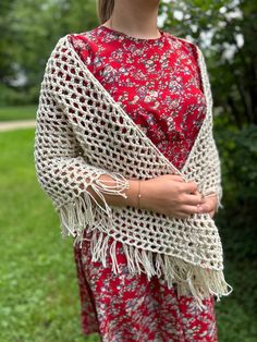 a woman standing in the grass wearing a red and white crochet shawl