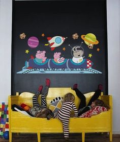 two children laying on a yellow couch in front of a chalkboard wall with the space theme