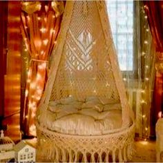 a white hanging chair in front of a window with lights on the curtained windowsill