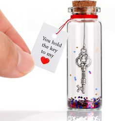 a person holding a key to a bottle with confetti on it and a tag that says you hold the key to my heart