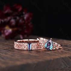 two rings with different colored stones sitting on top of a wooden table next to flowers