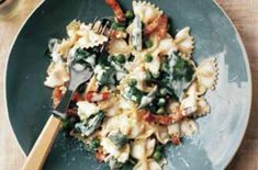 pasta with spinach and peas on a blue plate next to a glass of wine