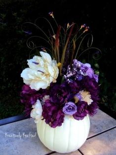 a white pumpkin vase filled with purple and yellow flowers