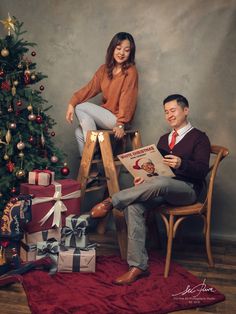 a man and woman sitting on stools in front of a christmas tree with presents