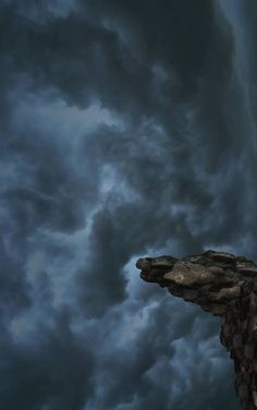 a man standing on top of a cliff under a cloudy sky