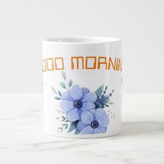 a white coffee mug with blue flowers and the words good morning written in orange on it