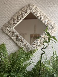 a mirror sitting on top of a white wall next to green plants and fern leaves