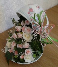 a white bucket with pink and white flowers in it sitting on a wooden table next to a wall