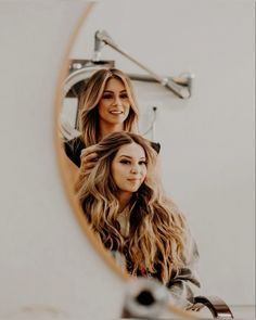 two women are looking at their reflection in the mirror while they both have long hair