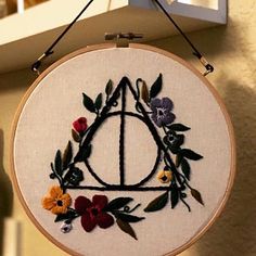 an embroidery project with flowers and leaves on the hoop hanging from a hook in front of a window