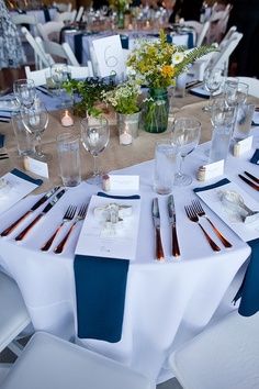 the table is set with white and blue linens, silverware, and flowers