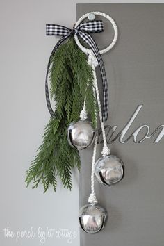 christmas decorations hanging from the side of a wall with pine branches and bells attached to it