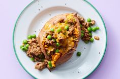 a white plate topped with a loaded baked potato covered in meat and peas on top of it