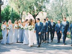 a group of people standing next to each other in front of trees and bushes at a wedding