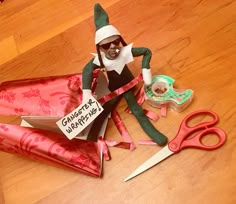 an elf sitting on the floor next to some wrapping paper and scissors