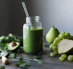 a green smoothie in a mason jar surrounded by fruit and vegetables