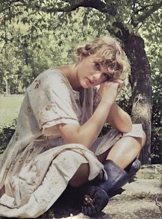 a woman sitting on the ground next to a tree with her head in her hands