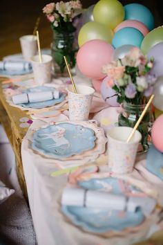 the table is set with plates, cups and vases filled with colorful balloons in pastel colors