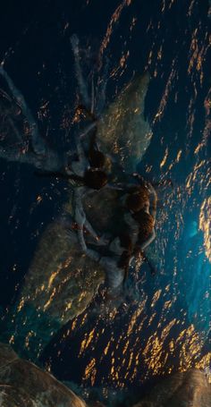 two people standing on rocks in the ocean at night with their backs turned to the camera