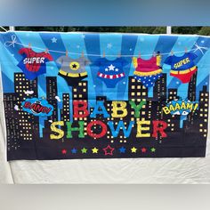 a baby shower banner hanging on a clothesline with city skylines and superhero symbols