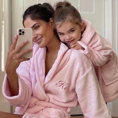 a woman taking a selfie with her daughter wearing pink robes and holding a cell phone