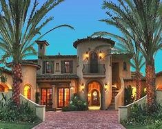 a large house with palm trees in the front yard and lights on it's windows